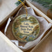 A decorative ornament in a box, featuring a scenic landscape with a lake, mountains, and a bird.