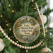 A round ornament hanging on a Christmas tree, featuring a scenic landscape with a lake, trees, and a bird.
