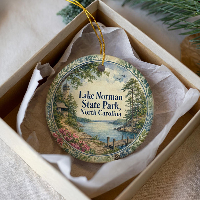 A decorative ornament in a box, featuring a scenic landscape with a lighthouse and a body of water.