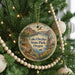 A round ornament hanging on a Christmas tree, featuring a scenic landscape with mountains, a lake, and wildlife.