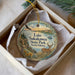 A decorative ornament in a white box, featuring a scenic landscape with a lake, a deer, and mountains in the background.