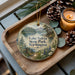 A wooden tray with a decorative ornament featuring a scenic landscape of Lake Sylvia State Park, Washington, surrounded by pine cones and a lit candle.