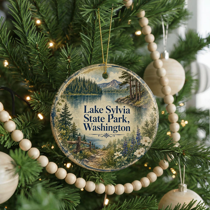 A round ornament hanging on a Christmas tree, featuring a scenic landscape with a lake, mountains, and trees.