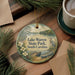 A decorative ornament with a lake and park scene, featuring a bird, a canoe, and pine trees, is displayed on a wooden surface alongside a cup of coffee and some papers.