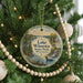 A round ornament hanging on a Christmas tree, featuring a scenic landscape with a lake, trees, and a waterfall.