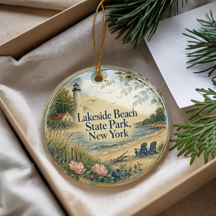 A decorative ornament with a lighthouse and beach scene, placed in a box with pine branches.