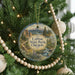 A round ornament hanging on a Christmas tree, featuring a scenic landscape with mountains, trees, and a river.