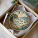 A decorative ornament in a box, featuring a scenic landscape with a lake, mountains, and a bird perched on a branch.