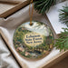 A round ornament with a scenic forest landscape and a bridge, placed inside a box with pine branches.