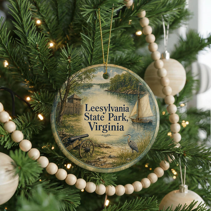 A round ornament hanging on a Christmas tree, featuring a scenic image of a lake, a sailboat, and a bird.