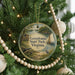 A round ornament hanging on a Christmas tree, featuring a scenic image of a lake, a sailboat, and a bird.
