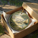 A round ornament in a box, featuring a scenic landscape with a river, a boat, and a bird, along with the text "Leesylvania State Park, Virginia".