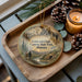 A wooden tray with a decorative ornament featuring a scenic landscape of Lewis and Clark's exploration of the Caves of State Park in Montana.