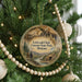 A Christmas ornament hanging on a tree, featuring a scenic landscape with mountains and a river.