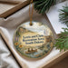 A round ornament with a scenic landscape featuring a river, mountains, and people in a canoe, hanging from a string.