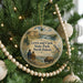 A circular ornament hanging on a Christmas tree, featuring a scenic landscape with a buffalo and a couple of people.