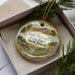 A decorative ornament featuring a scenic landscape of Little Missouri State Park, North Dakota, with mountains, a river, and a cabin in the background.