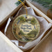 A decorative ornament in a box, featuring a scenic landscape with a house, bridge, and trees, along with the text "Lockhart State Park, Texas".