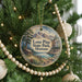 A round ornament on a Christmas tree, featuring a scenic landscape with mountains, pine trees, and a cabin.
