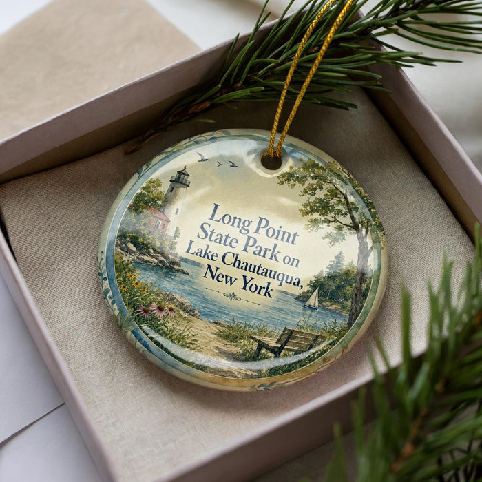 A decorative ornament with a lighthouse and a scenic lake in the background, placed in a box with pine branches.