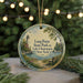 A round ornament with a lighthouse and a bench, surrounded by greenery, is displayed in front of a blurred background with twinkling lights.