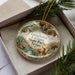 A decorative ornament in a box, featuring a scenic landscape with a cow and trees, along with the text "Longhorn Canyon State Park, Texas".