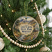 A round ornament hanging on a Christmas tree, featuring a scenic landscape with mountains, trees, and a stream.