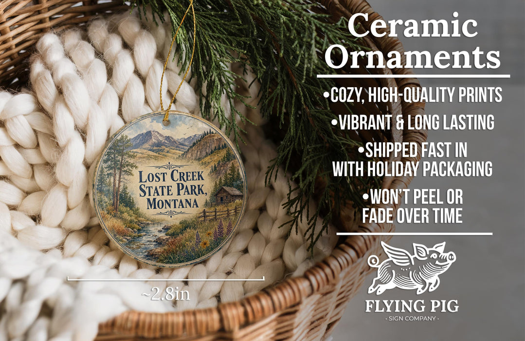 Ceramic ornaments, specifically a Lost Creek State Park ornament, are displayed in a basket with pine branches. The ornament features a scenic image of the park and includes text describing the ornament's features.