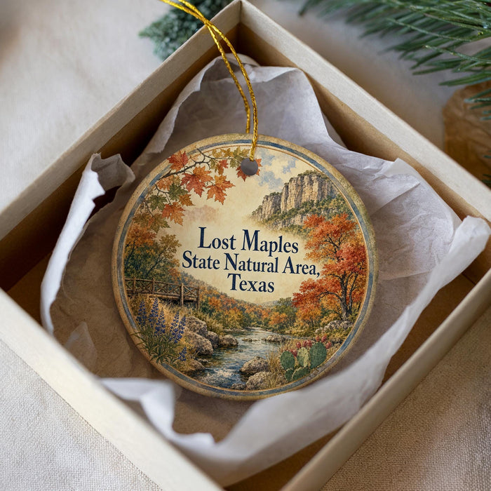 A decorative ornament in a box, featuring a scenic landscape with a river, mountains, and fall foliage.