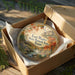 A decorative ornament in a box, featuring a scenic landscape with a river, mountains, and autumn foliage.
