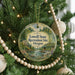 A round ornament hanging on a Christmas tree, featuring a scenic landscape with a bridge and trees.