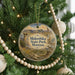 A round ornament hanging on a Christmas tree, featuring a scenic landscape with mountains, trees, and a bird in flight.