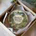 A decorative ornament in a box, featuring a scenic landscape with a lake, pine trees, and a cabin, with the text "Manchester State Park, Washington" prominently displayed.