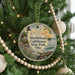 A round ornament hanging on a Christmas tree, featuring a lighthouse and a scenic landscape.