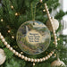 A round ornament hanging on a Christmas tree, featuring a scenic landscape with a waterfall and a bridge.