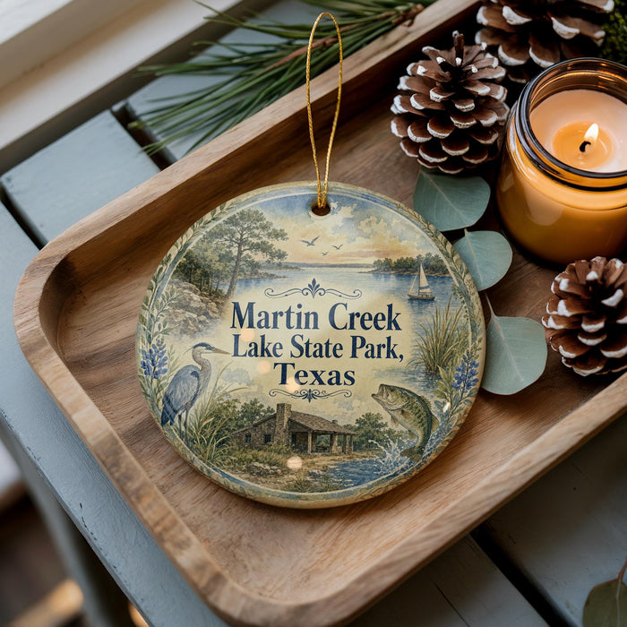A decorative ornament with a painting of Martin Creek Lake State Park, Texas, sits on a wooden tray alongside pine cones and a lit candle.