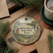 A round ornament with a scenic illustration of Martin Dies Jr. State Park, Texas, is displayed on a wooden surface alongside a cup of coffee and some pine branches.