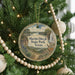 A round ornament hanging on a Christmas tree, featuring a scenic landscape with a waterfall and a deer.