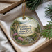A round ornament with a scenic image of a park, featuring a river, trees, and flowers, is displayed in a box with pine branches.