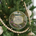 A round ornament hanging on a Christmas tree, featuring a scenic image of a park with a river and mountains.
