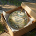 A decorative ornament in a wooden box, featuring a scenic landscape with a river, waterfall, and wildlife.