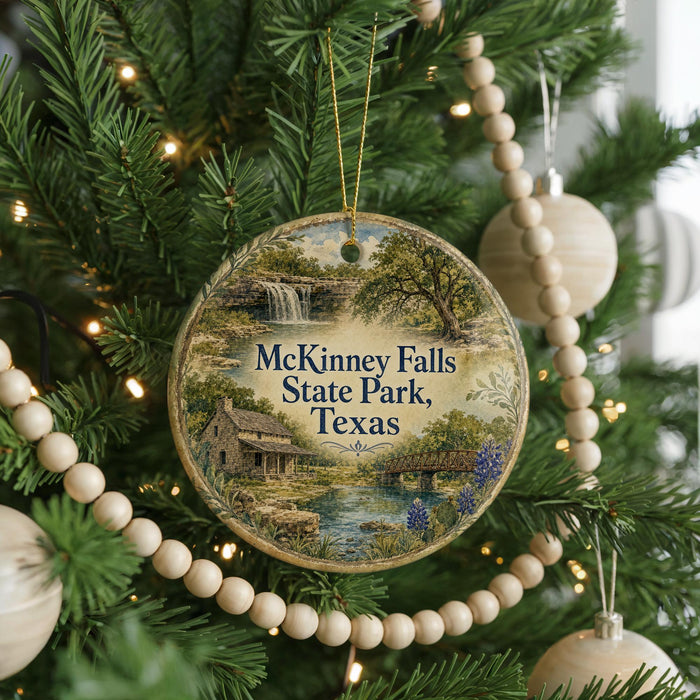 A circular ornament hanging on a Christmas tree, featuring a scenic landscape with a waterfall and a cabin.