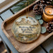 A wooden tray with a decorative ornament featuring a scenic landscape of Medicine Rocks State Park, Montana, and pine cones.