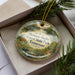 A decorative ornament in a box, featuring a scenic image of Tennessee State Park, with pine branches and greenery surrounding it.