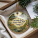 A decorative ornament with a scenic forest landscape, featuring a deer, a bird, and a canoe, is displayed in a box with pine branches.