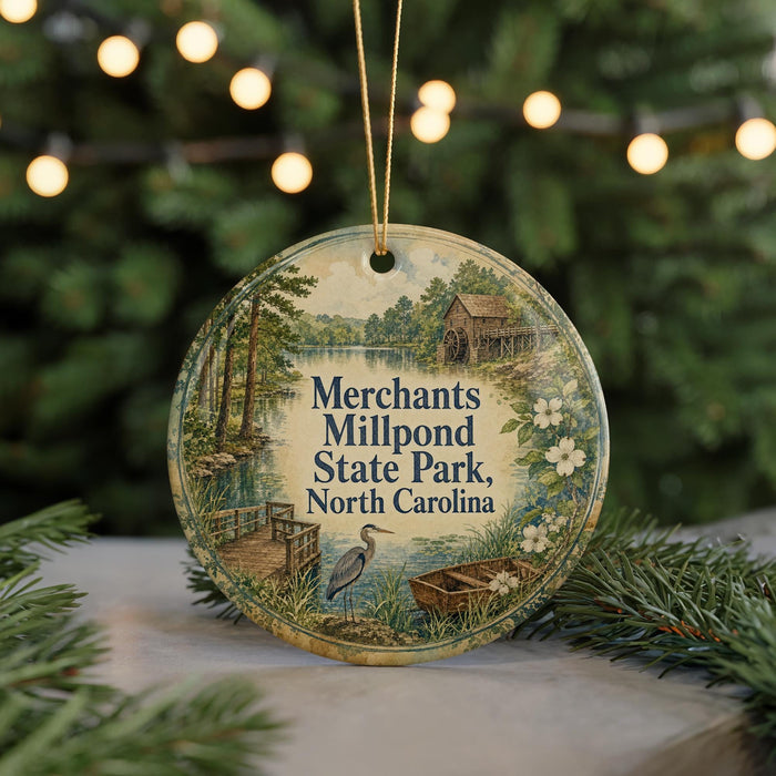 A round ornament with a scenic image of Mill Pond State Park in North Carolina, featuring a bird, a wooden cabin, and a boat on the water.