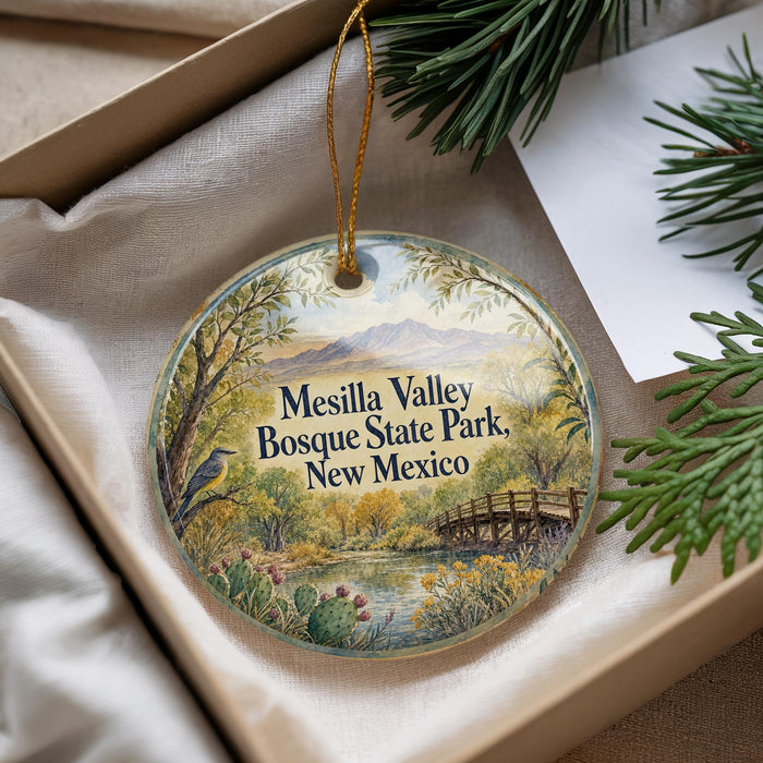 A decorative ornament with a scenic landscape of Mesilla Valley, Bosque State Park, New Mexico, featuring a bird perched on a tree branch and a bridge in the background.
