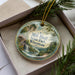A decorative ornament with a scenic landscape of Mill Bluff State Park, Wisconsin, featuring a waterfall and pine trees.
