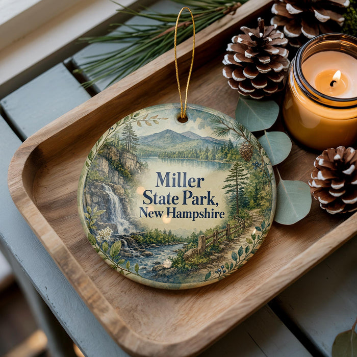 A decorative ornament featuring a scenic landscape of Miller State Park in New Hampshire, with pine cones and a lit candle on a wooden tray.