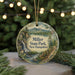A round ornament with a scenic landscape of a waterfall, pine trees, and mountains, hanging from a string.